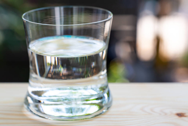 Vidrio transparente de agua limpia en mesa de madera en fondo de jardín bokeh, Close up & Macro shot, enfoque selectivo, concepto de bebida saludable
 - Foto, imagen