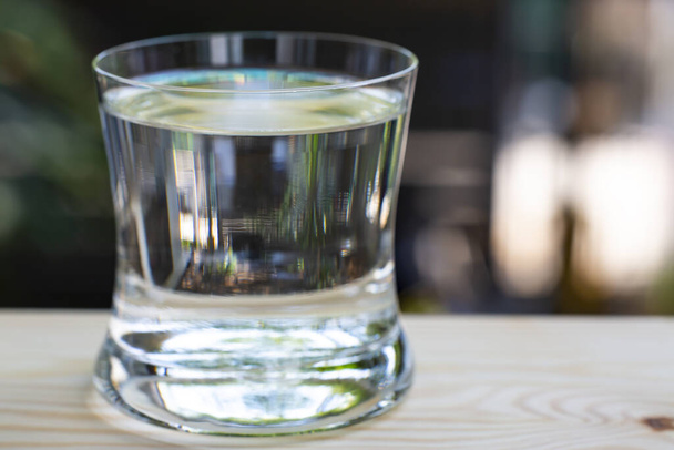 Transparent glass of clean water on wood table in bokeh garden background, Close up & Macro shot, Selective focus, Healthy Drink concept - Photo, image