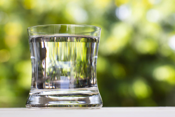 Transparent glass of clean water on wood table in bokeh green garden background, Close up & Macro shot, Selective focus, Healthy Drink concept - Zdjęcie, obraz