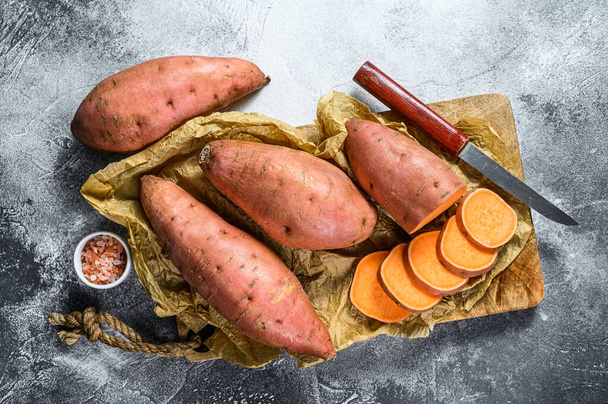 Raw sweet potatoes on a chopping Board, organic yam. Farm vegetables. Gray background. - Fotografie, Obrázek