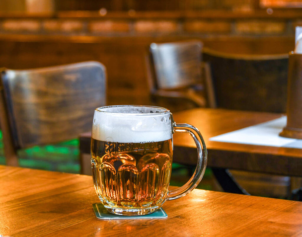 PRAGA, REPÚBLICA CHECA - JULIO 2018: Un vaso de cerveza pilsner lager checa espumosa sobre una mesa de madera en un bar de Praga
 - Foto, Imagen