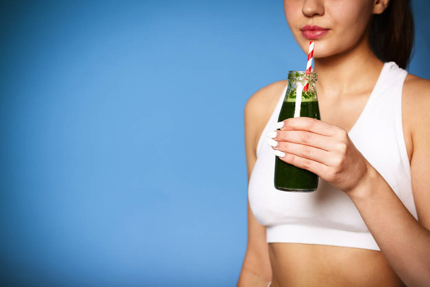 Crop delighted young woman with green smoothie laughing against wall background - Photo, Image