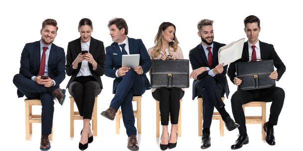Team of 6 businessmen talking on phone, holding newspaper and briefcase while sitting on chairs on white studio background - Photo, Image