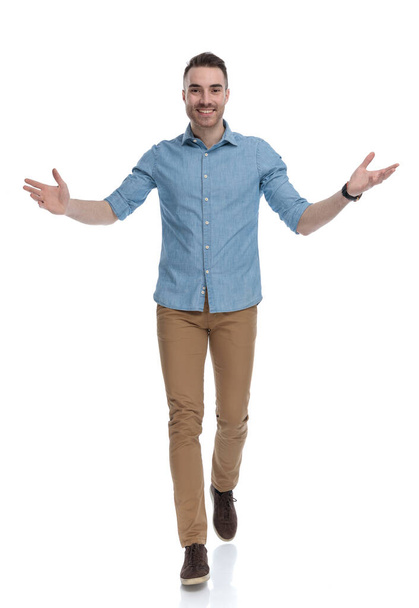 Cheerful casual man smiling and welcoming while wearing blue shirt, stepping on white studio background - Foto, Imagen