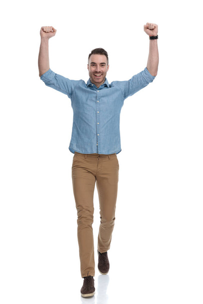 Cheerful casual man celebrating and laughing while wearing blue shirt, walking on white studio background - Photo, Image