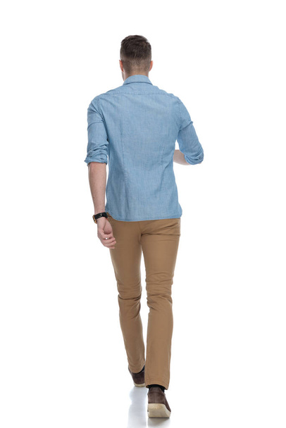 Vue arrière d'un homme décontracté confiant portant une chemise bleue, marchant sur fond de studio blanc
 - Photo, image