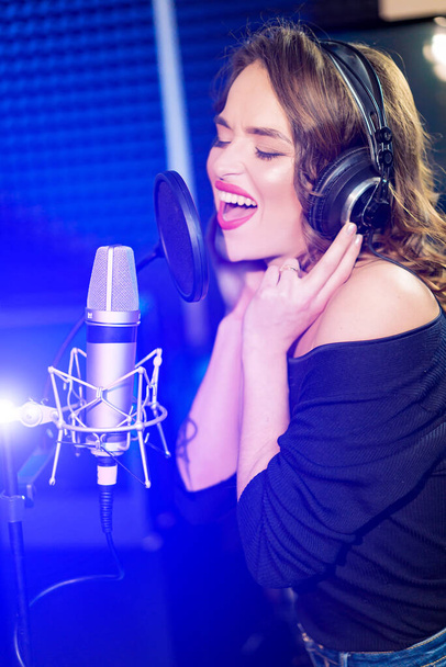 Shot of a pretty young woman in headphones singing a song with a microphone. Shot in a studio. Vocalist female portrait - Φωτογραφία, εικόνα