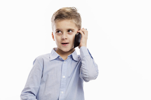 A school boy in a blue shirt is talking on the phone. Isolated on a white background. - Foto, afbeelding