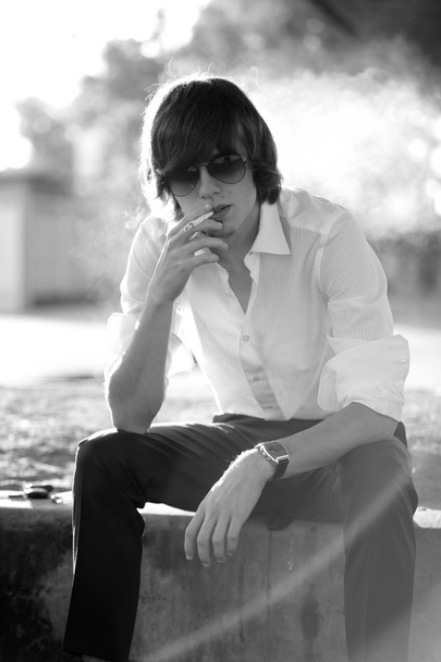 Handsome man in white shirt smoking while sitting on street - Foto, afbeelding
