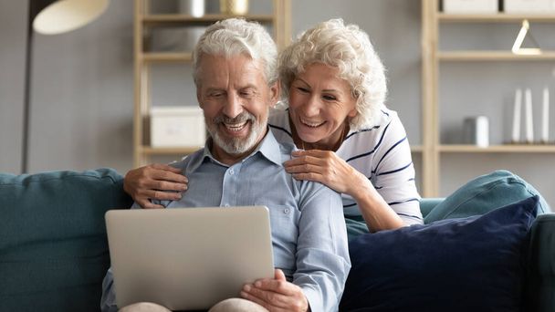 Happy middle-aged couple relax at home using laptop - 写真・画像
