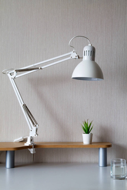 office interior. white lamp with a small plant with glass of water on a white table. desktop organization. - Фото, зображення