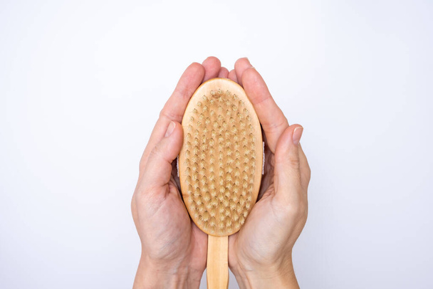 A wooden brush for dry body anti-cellulite massage and peeling skin in female hands on white background. - Foto, immagini