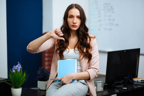 business woman sitting at desk showing thumb down
. - Фото, изображение