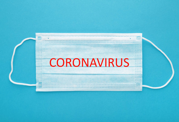 Medical mask on blue background. The inscription Coronavirus, top view - Foto, afbeelding