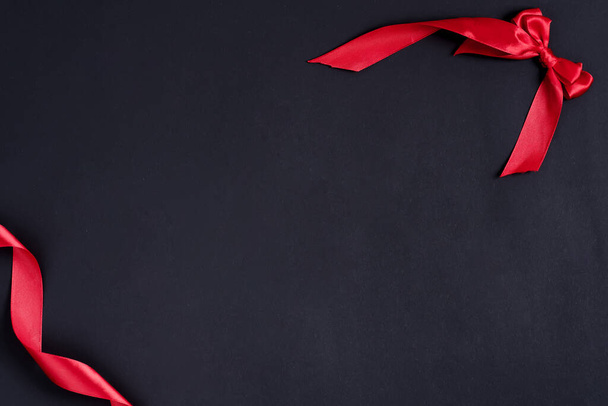 Праздничный черный фон с угловой рамкой из красной ленты и декоративным бантом
. - Фото, изображение