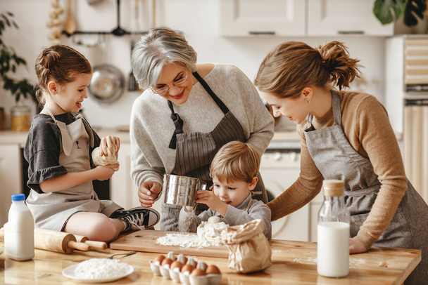 familia feliz una abuela con su hija y nietos cocina en la cocina, amasa la masa y hornea galletas
 - Foto, imagen