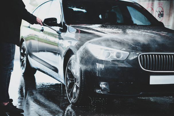Egy felnőtt férfi kezei, amint kint mossa a kocsiját egy autómosóban, nagy nyomású víz alatt. - Fotó, kép