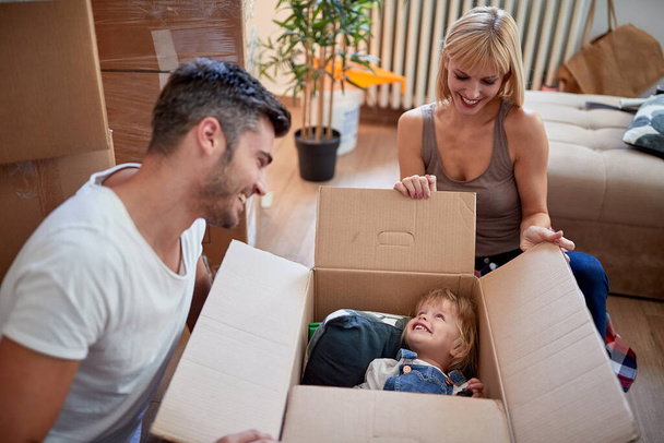 rodiče si hrají se svou dcerou schovanou v kartonové krabici v novém bytě. nový byt, nový začátek, radost, hravý, bezstarostný, volný čas koncept - Fotografie, Obrázek