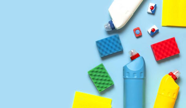 House cleaning concept. Household chemicals, disinfectant, bleach, antibacterial gel, yellow rubber gloves, sponge, rags, dishwasher tablets on blue background. Flat lay top view. Cleaning accessories. - Photo, Image
