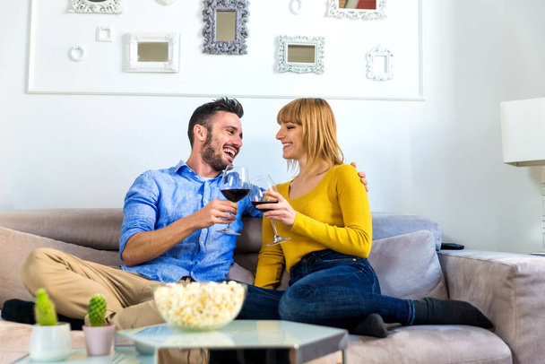 Two young adults at home - Beautiful couple relaxing and watching a movie at tv - Foto, Imagem