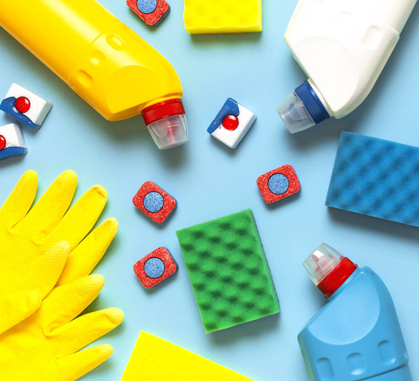 House cleaning concept. Household chemicals, disinfectant, bleach, antibacterial gel, yellow rubber gloves, sponge, rags, dishwasher tablets on blue background. Flat lay top view. Cleaning accessories - Photo, Image