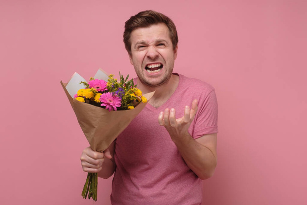 Сердитий коханець або зламаний сердечний чоловік в рожевому одязі, що стоїть з квітковим букетом
. - Фото, зображення