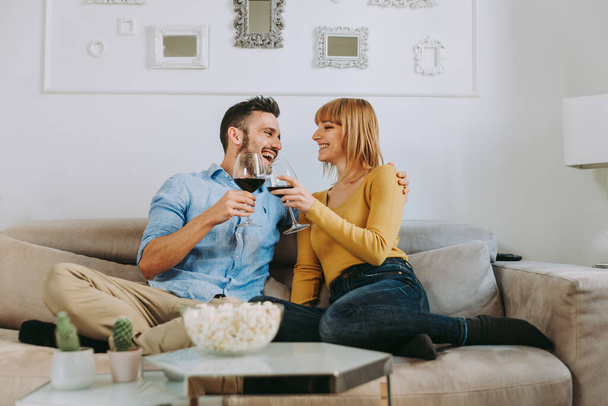 Two young adults at home - Beautiful couple relaxing and watching a movie at tv - Фото, изображение