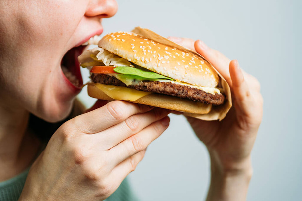 La chica sostiene una hamburguesa con las manos y la muerde. De cerca.
. - Foto, Imagen