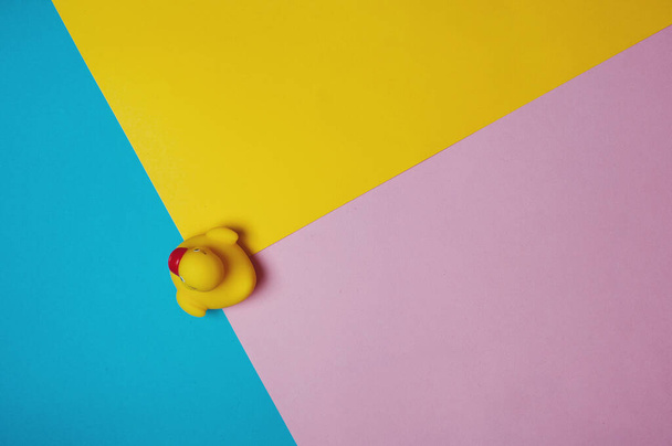 Gele rubberen eend op blauwe, roze en gele achtergrond. Bad concept. Kopieerruimte, platte lay. - Foto, afbeelding