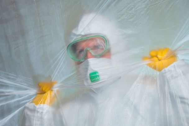 Worried exhausted epidemiologist trapped behind plastic curtain in virus quarantine, medical professional in protective clothing, selective focus - Foto, Bild