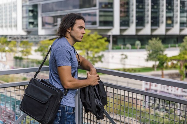 Traurig aussehender Mann mit großer schwarzer Brieftasche lehnt nachdenklich an einem Metallgeländer vor einem städtischen Gebäude - Foto, Bild