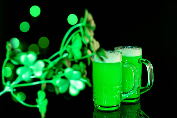 Ημέρα του Αγίου Πατρικίου πράσινη μπύρα με φύλλα τριφύλλι στο μαύρο ανακλαστικό φόντο. Σχέδιο τέχνης, ωραία φώτα, bokeh. Γιορτάζοντας την Ημέρα του Αγίου Πατρικίου εθνικό παραδοσιακό φεστιβάλ. - Φωτογραφία, εικόνα