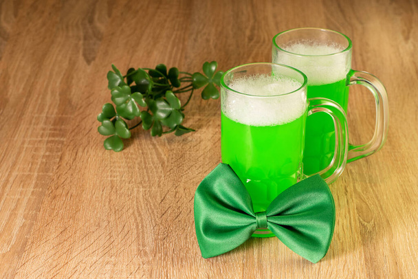 Green beer, bow tie and a branch of shamrock on the wooden background closeup. Symbols of traditional irish festival St. Patrick's Day.  - Photo, Image