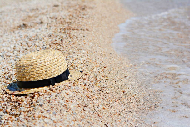Ψάθινο καπέλο στην άμμο, αντιηλιακό. Γυναικεία αξεσουάρ παραλίας ή καλοκαιρινό ντύσιμο σε αμμώδη φόντο. - Φωτογραφία, εικόνα
