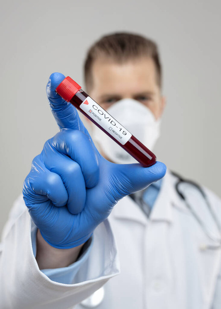 Doctor wearing respiratory mask and holding the Coronavirus Covid-19 blood sample  - Valokuva, kuva