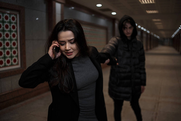 a young beautiful woman walks through the underpass at night, followed by a man. the male robber pulls the girl's hand,the girl calls the rescue service and tries to escape - Photo, Image