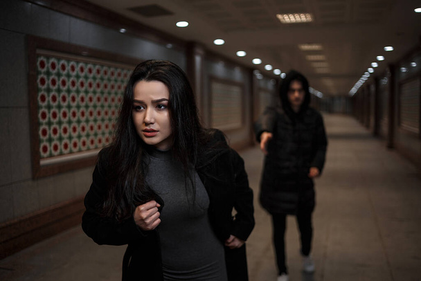 una joven mujer hermosa trata de escapar de un ladrón con ropa negra. en el paso subterráneo. por la noche
 - Foto, imagen