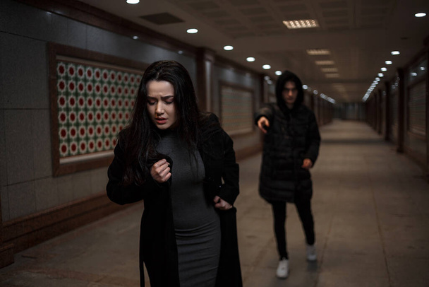 una joven mujer hermosa trata de escapar de un ladrón con ropa negra. en el paso subterráneo. por la noche
 - Foto, imagen