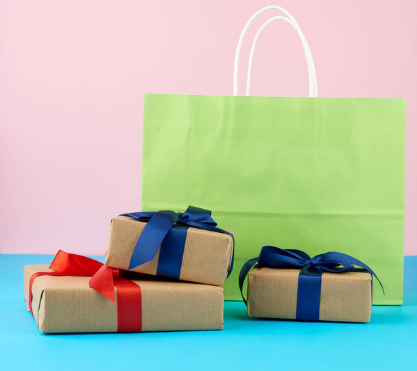 ギフト付きの茶色い紙箱と、ショッピング用の多色の紙袋、ピンクブルーの背景に白い柄のギフトが立つ - 写真・画像