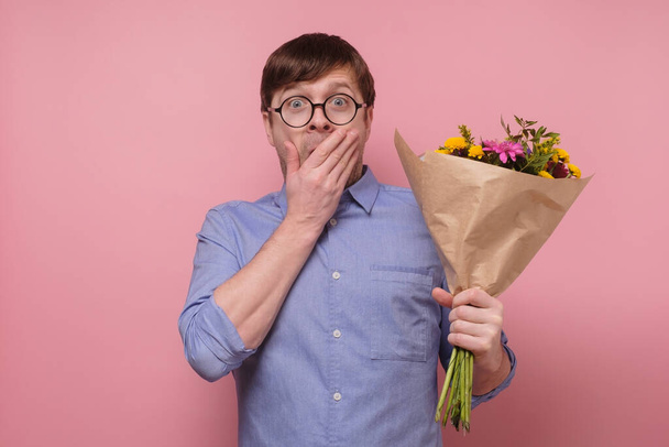 Jovem caucasiano em óculos tendo surpreendido o rosto com flores para sua namorada
 - Foto, Imagem