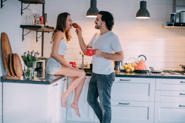自宅のキッチンで朝の若い愛情のカップル。男と女は美しいスタイリッシュなキッチンで楽しい朝食を持っています. - 写真・画像