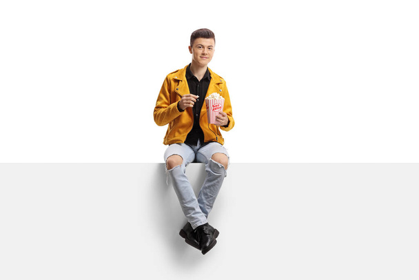 Young guy on a panel eating popcorn isolated on white background - Zdjęcie, obraz