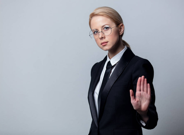 Mujer de negocios de estilo en un traje de negocios negro clásico y gafas muestran gesto de parada
  - Foto, Imagen