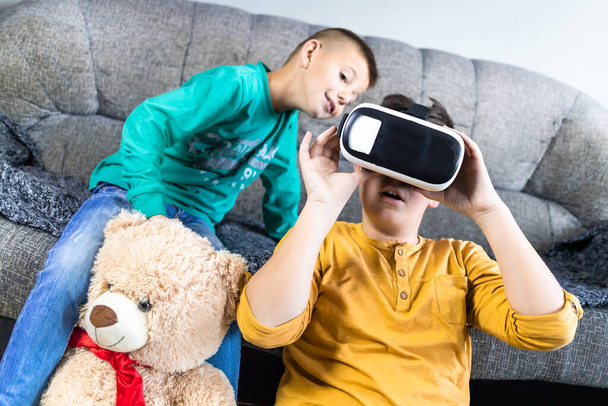 Cute, little boy having fun with vr headset with his brother next to him and teddy bear toy. Kids and technology concept - Fotó, kép