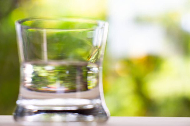 Blurred transparent glass of clean water on wood texture in bokeh green garden background, Close up & Macro shot, Selective focus, Healthy Drink concept - Photo, Image