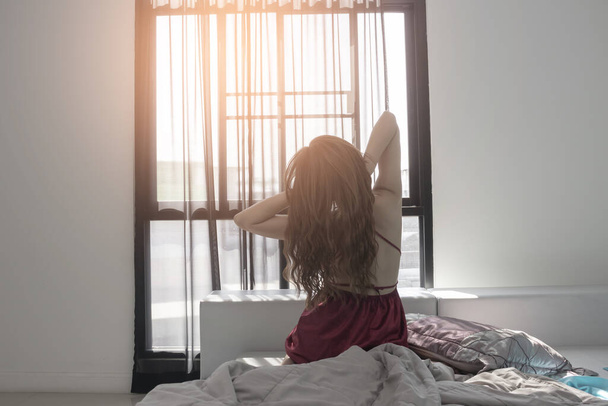 Femme s'étendant au lit après le réveil, vue arrière, entrant dans une journée heureuse et détendue après une bonne nuit de sommeil
 - Photo, image
