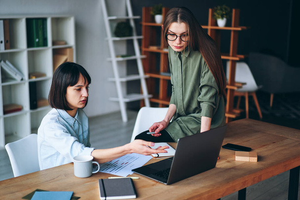 Two serious businesswomen having a meeting using laptop in minimalist office - Fotoğraf, Görsel