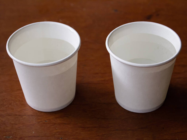 Dos tazas de papel de agua sobre fondo de mesa de madera, Primer plano y macroplano
 - Foto, Imagen