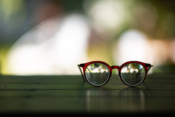 Braune Brille mit Holztisch, Im bokeh grünen Gartenhintergrund, Nahaufnahme & Makroaufnahme, Selektiver Fokus, Optisches Konzept - Foto, Bild