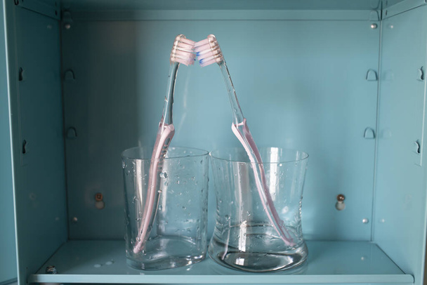 Zwei rosa Zahnbürsten in 2 feuchtem Glas auf blauem Metallschrank, Über Lgbt Lifestyle, Badezimmerkonzept - Foto, Bild